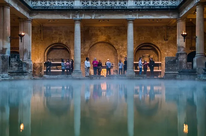 Steam rising from the green water of the Great Bath below a colonnade lit by torches