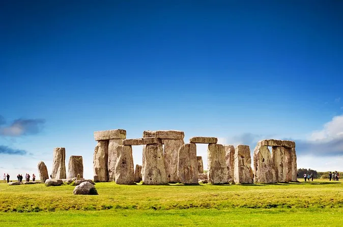 The Stonehenge circle under a deep blue sky with a few visitors on the path